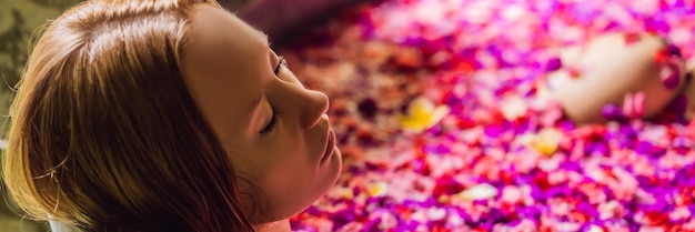 Atractiva mujer joven en el baño con pétalos de flores tropicales y tratamientos de spa con aceites aromáticos para
