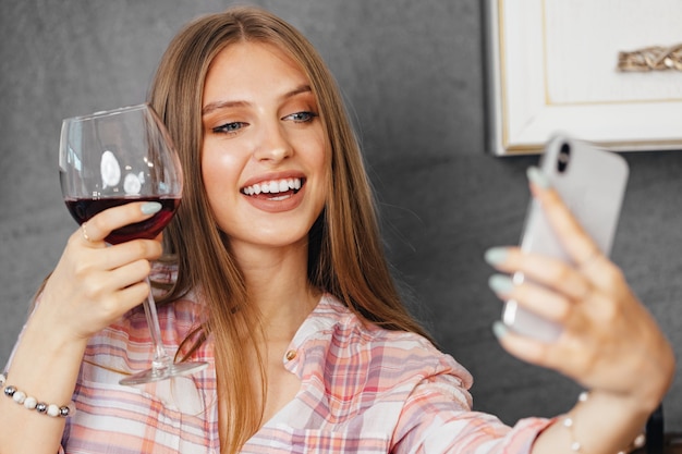 Foto atractiva mujer joven bebiendo vino y con smartphone en la cocina, retrato