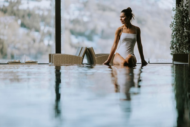 Atractiva mujer joven en bikini se sienta junto a la piscina en la piscina cubierta en invierno
