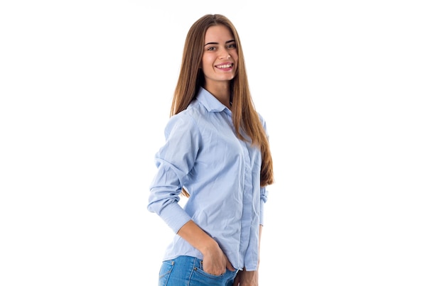 Atractiva mujer joven con cabello castaño largo vistiendo una camisa azul sobre fondo blanco en estudio