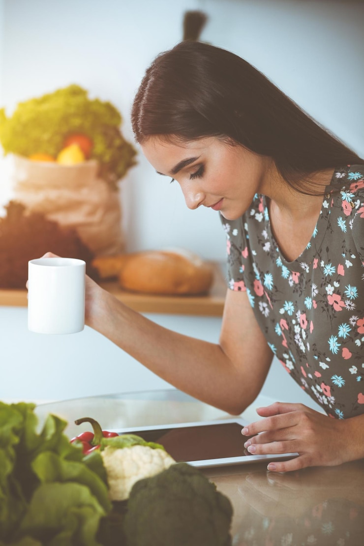 Foto una atractiva mujer joven de cabello oscuro bebiendo café por la mañana y buscando una nueva receta para una deliciosa comida mientras está sentada en la cocina soleada tablet pc es el mejor libro de cocina
