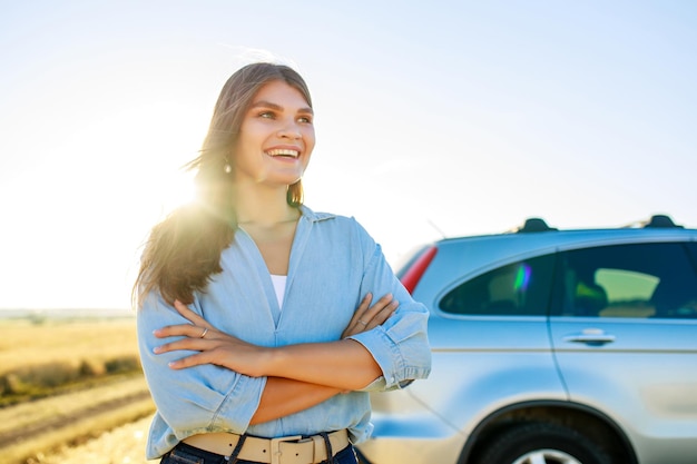 Atractiva mujer joven con camisa azul a la luz del atardecer con su auto