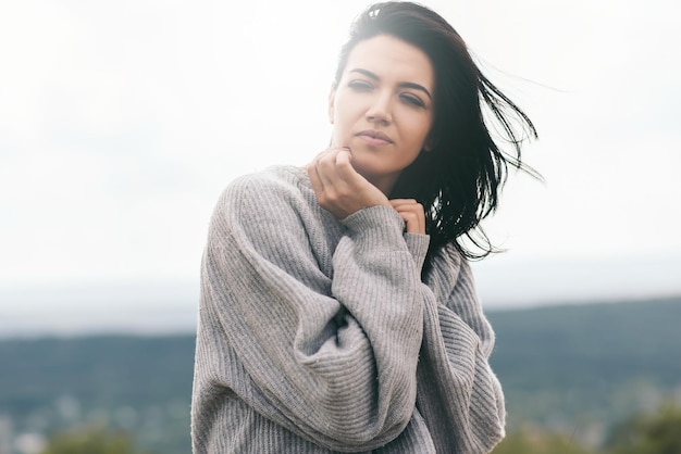 Atractiva mujer joven caucásica morena con cabello ventoso afuera contra el cielo y la naturaleza Retrato de mujer de ensueño con los ojos cerrados con la mano en la cara Concepto de moda de estilo de vida Estado de ánimo de idea de portada