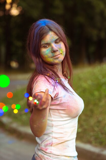 Atractiva mujer joven cubierta con coloridos polvos Holi con guirnalda