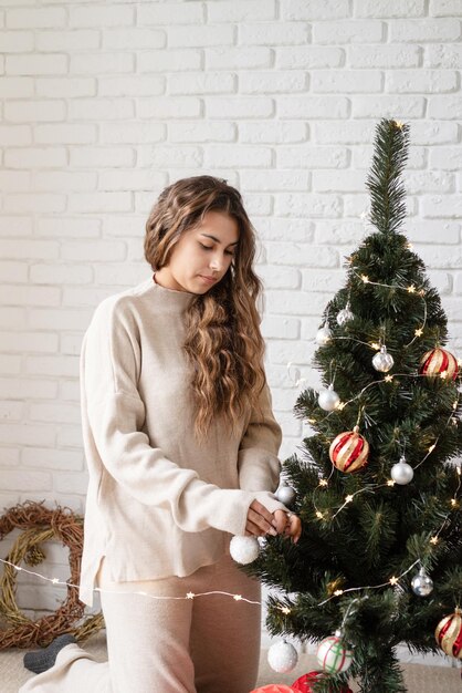 Atractiva mujer joven decorar el árbol de Navidad con luces de colores