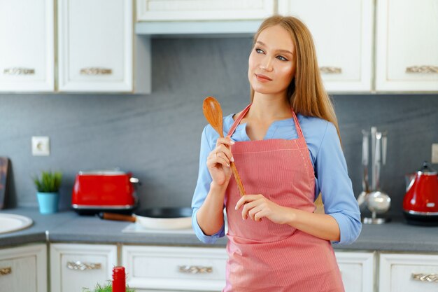 Atractiva mujer joven en delantal rojo de pie en su cocina