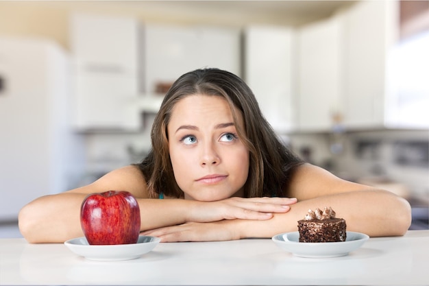 Atractiva mujer joven elige entre manzana y pastel, concepto de estilo de vida saludable