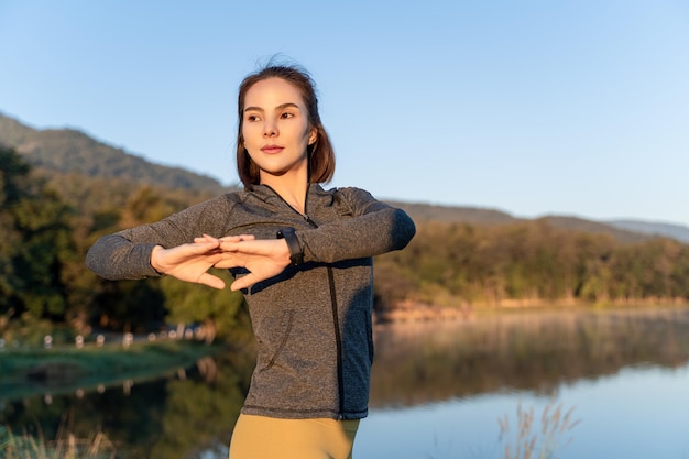 Atractiva mujer joven estirando los brazos y las piernas antes de su ejercicio matutino en un parque local con el cielo del amanecer matutino y el fondo de las montañas