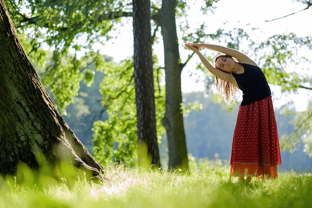 Atractiva mujer joven con falda roja está practicando yoga y haciendo asana por la mañana