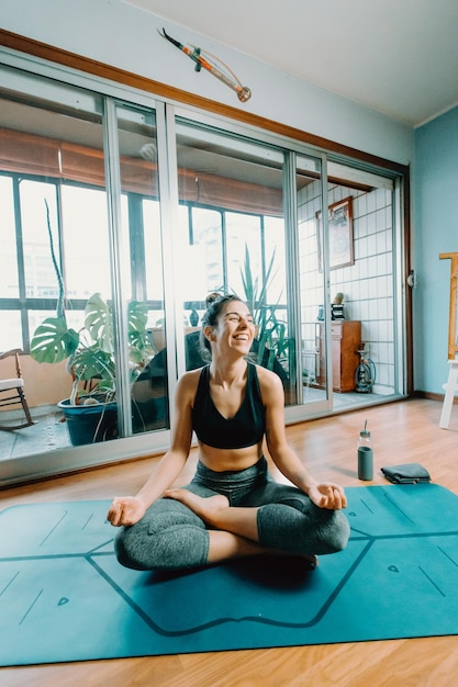 Atractiva mujer joven en forma sentada en una pose de loto haciendo yoga con clase en línea en casa. Entretenimiento y educación en Internet. Concepto de estilo de vida saludable durante el tiempo libre. sonriendo a la cámara