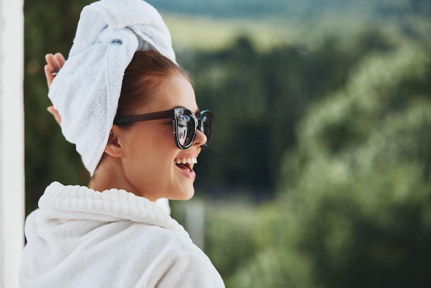 Atractiva mujer joven con gafas de sol posando en una bata de baño en un descanso de balcón Estilo de vida