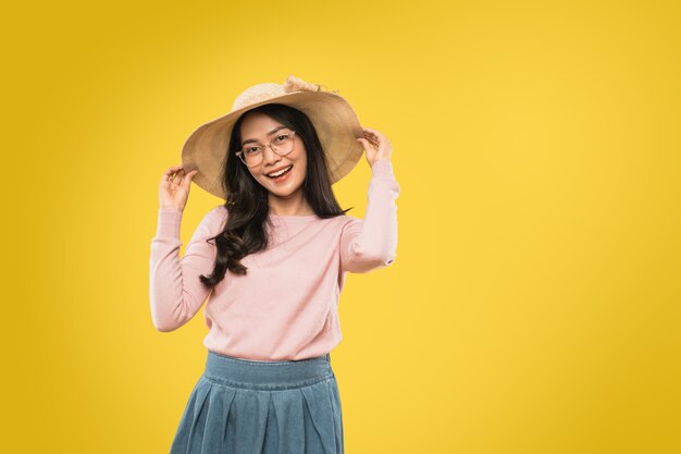 Atractiva mujer joven con gafas sonriendo con ambas manos sosteniendo el sombrero