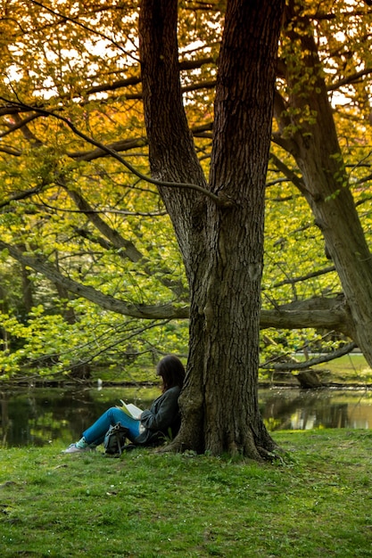 Atractiva mujer joven leyendo un libro mientras se sienta en el césped en un parque público verde Primavera al aire libre Unidad verde con la naturaleza Pasar tiempo libre al aire libre