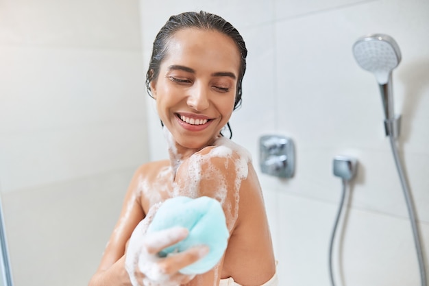 Atractiva mujer joven con lufa de baño mientras toma ducha