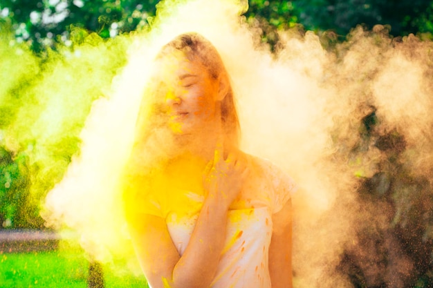 Atractiva mujer joven de pie en una nube de pintura Holi