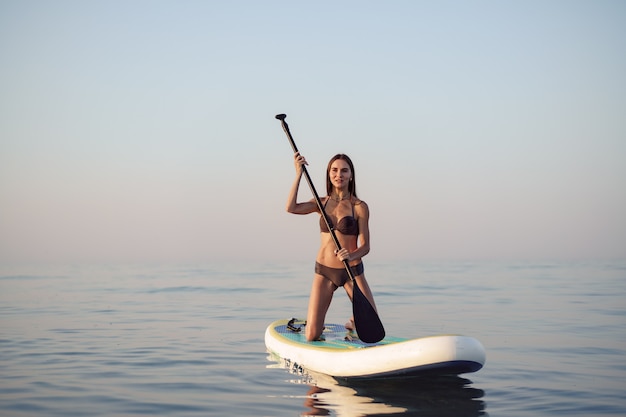 Atractiva mujer joven de pie en paddle board al amanecer.