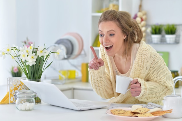 Atractiva mujer joven con portátil en la cocina