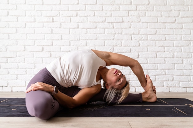 Atractiva mujer joven practicando yoga mientras usa ropa deportiva en el interior