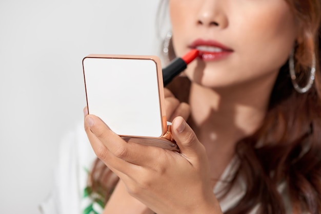 Atractiva mujer joven refrescando su lápiz labial de maquillaje sosteniendo una caja de polvo de espejo de mano en un día soleado