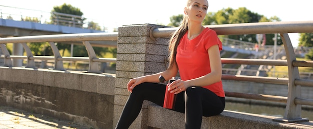 Atractiva mujer joven con ropa deportiva tomando un descanso mientras se sienta al aire libre.