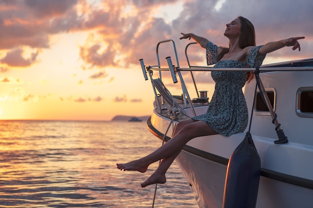 Atractiva mujer joven sentada en la cubierta del yate y disfrutando del atardecer