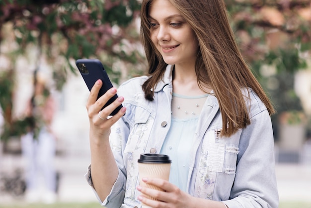 Atractiva mujer joven con smartphone y una taza de café en las manos sobre el fondo del árbol de sakura