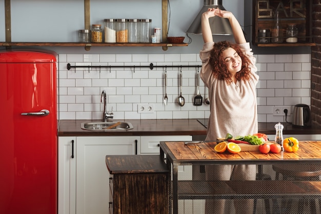 Foto atractiva mujer joven sonriendo mientras cocina ensalada con verduras frescas en el interior de la cocina en casa