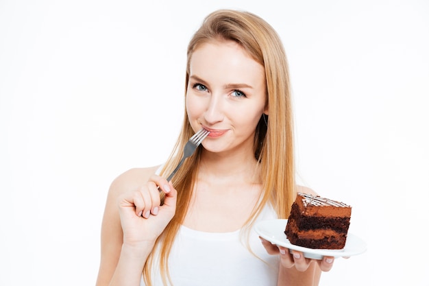 Atractiva mujer joven sonriente comiendo un trozo de tarta de chocolate sobre fondo blanco.