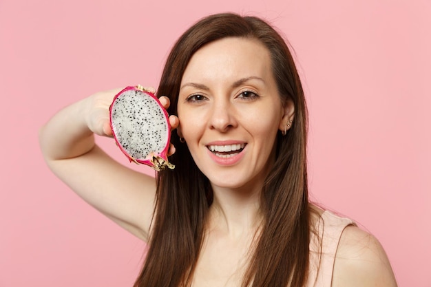 Atractiva mujer joven sosteniendo en la mano la mitad de pitahaya madura fresca, fruta de dragón aislada en el fondo de la pared rosa pastel en el estudio. El estilo de vida vívido de la gente relaja el concepto de vacaciones. Simulacros de espacio de copia.