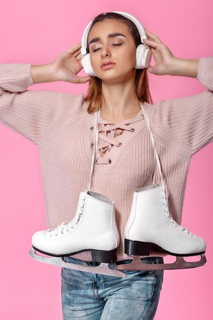 Atractiva mujer joven sosteniendo patines para hielo y escucha música en auriculares