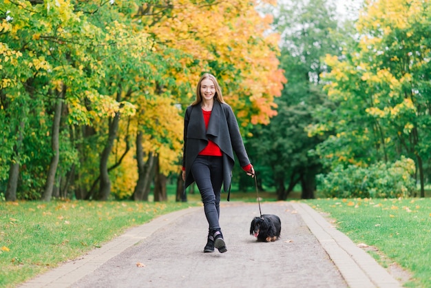 Atractiva mujer joven sosteniendo su perro dachshund en sus brazos al aire libre al amanecer en el parque en otoño