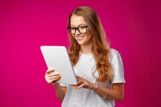 Atractiva mujer joven con tableta digital blanca sobre fondo rosa