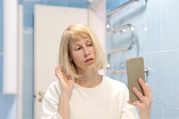 Atractiva mujer joven tomando selfie con smartphone en el baño.