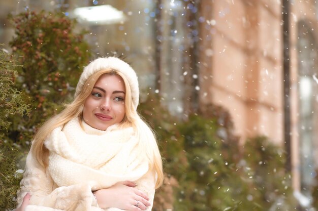 Atractiva mujer joven en traje de invierno caminando cerca de las piceas en la ciudad