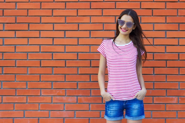 Atractiva mujer joven vestida con una camiseta de rayas rojas y blancas posando sobre un fondo de una pared de ladrillo rojo