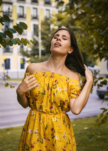 Atractiva mujer joven con un vestido floral amarillo de pie entre árboles