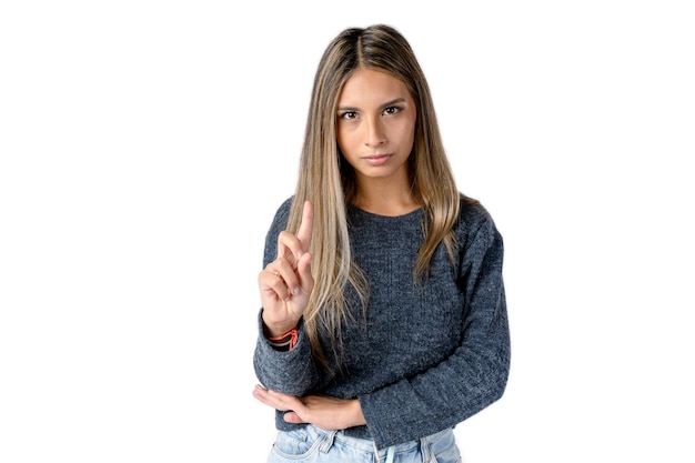 Atractiva mujer latina con una expresión enojada o seria haciendo un signo de NO con su dedo índice sobre un fondo blanco puro. Estudio fotográfico.