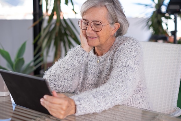 Atractiva mujer mayor que usa tableta digital sentada al aire libre mujer canosa sonriente mirando páginas web