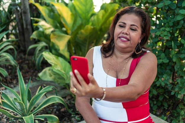 Atractiva mujer mayor sonriente tomando una foto en su teléfono inteligente mientras se sienta sola en un parque público