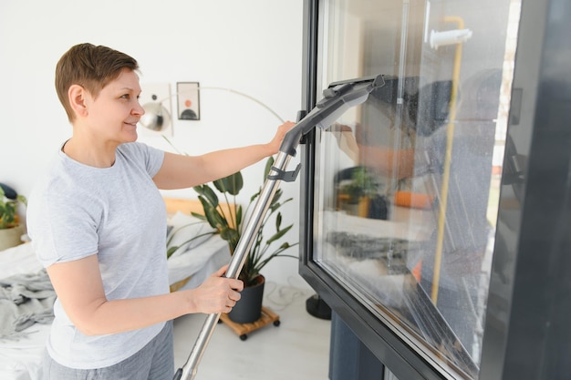 Una atractiva mujer de mediana edad está lavando una ventana en una habitación.