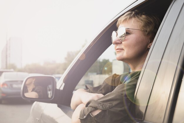 Atractiva mujer de mediana edad con gafas de sol mira por la ventana de su auto