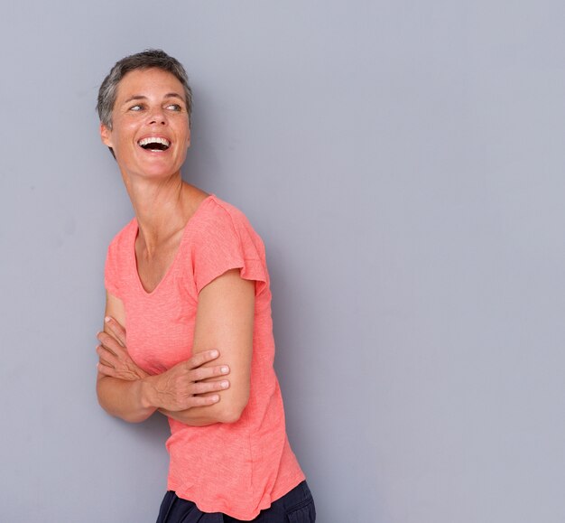 Atractiva mujer de mediana edad riendo contra una pared gris.