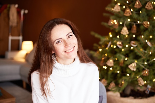 Atractiva mujer milenaria sentada en una silla en un salón decorado árbol de Navidad con decoración en el fondo