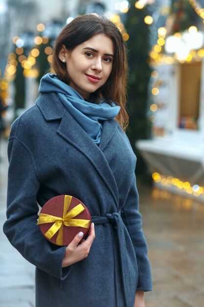 Atractiva mujer morena con caja de regalo cerca de la feria de Navidad