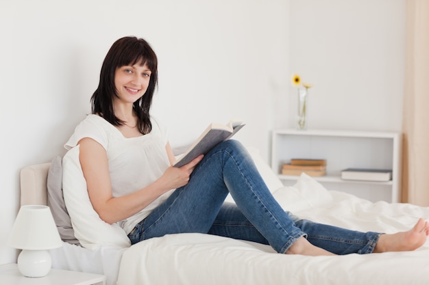 Atractiva mujer morena leyendo un libro mientras está sentado en una cama