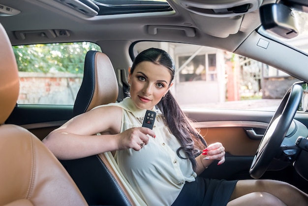 Atractiva mujer morena con llave de coche posando dentro del coche