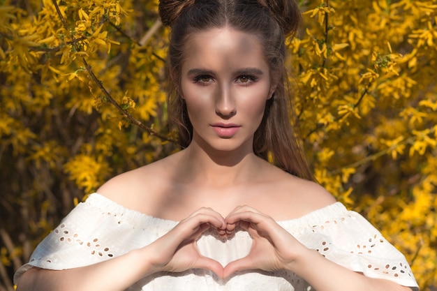 Atractiva mujer morena con maquillaje hermoso que muestra en forma de corazón en sus manos