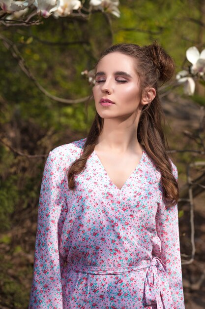 Atractiva mujer morena posando cerca del árbol de magnolia en flor en vestido de moda