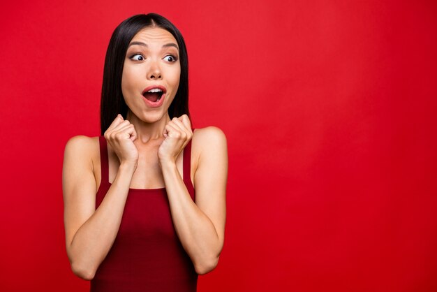 Atractiva mujer morena con un vestido rojo posando contra la pared roja