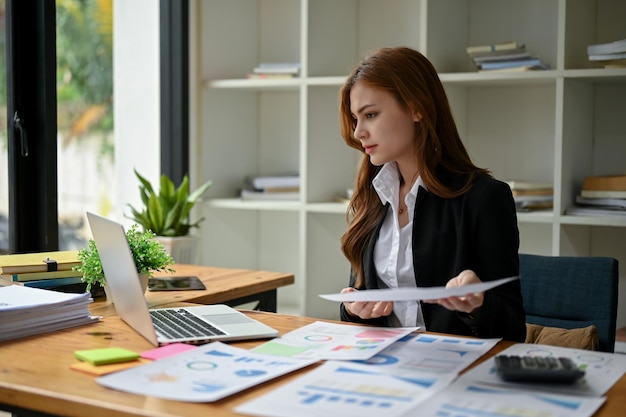 Una atractiva mujer de negocios asiática se enfoca en sus informes financieros usando una laptop